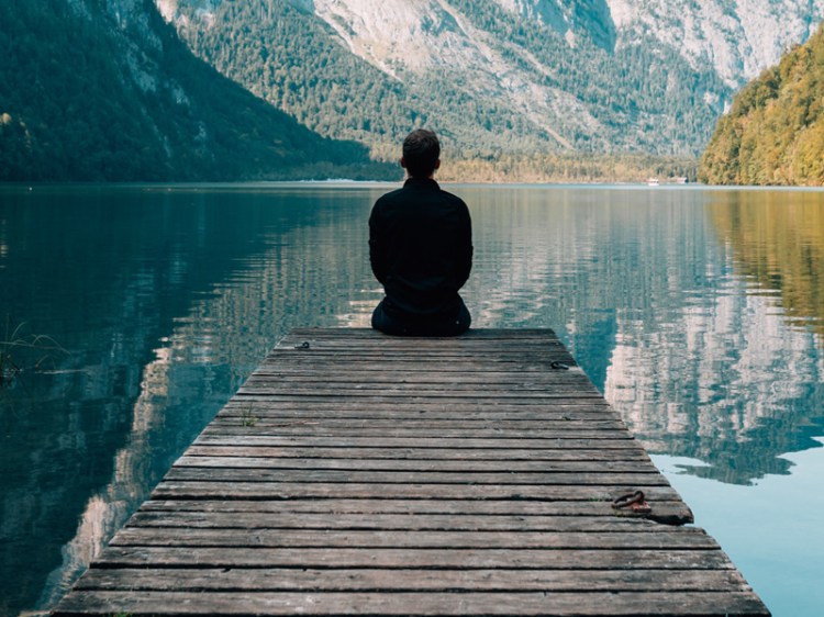 man sitting on a bridge by a lake with the mountain view